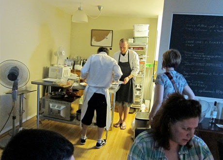 Chefs Damian and Steve work in the background preparing the next delicious offering to guests at NFA underground restaurant. On the wall to the right you can see a chalkboard describing the six course set menu offering.